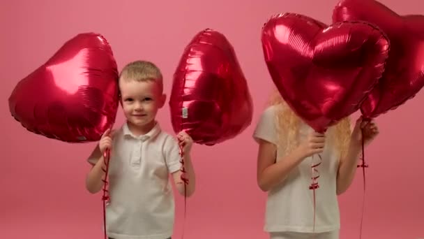 Zabawne dzieci bawią się w Walentynki lub Dzień Matki, trzymając w rękach balony w kształcie serca, bawiąc się, uśmiechając i grając emocjonalnie. — Wideo stockowe