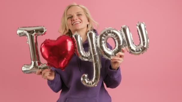 Счастливая 30-летняя женщина улыбается и танцует держа гелиевый шар с надписью Я ЛЮБЛЮ ВАС поздравляю с Днем Матери или Днем Святого Валентина. — стоковое видео