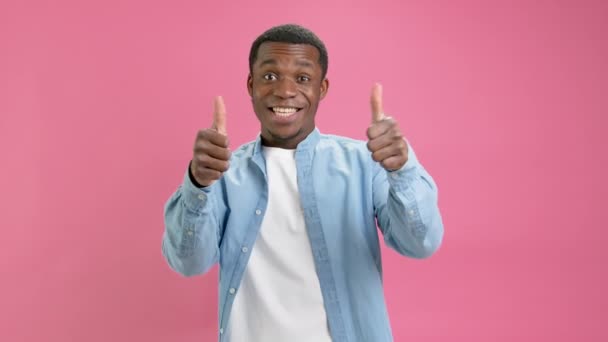 Selbstbewusster Führer, junger Afroamerikaner in Jeanshemd und weißem T-Shirt, macht ermutigende Daumen-nach-oben-Gesten, Daumen-nach-oben, als Geste isoliert auf einfachem rosa Studiohintergrund. — Stockvideo