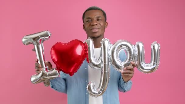 Afro-americano feliz no amor em camisa jeans expressa suas emoções de amor, detém palavra vermelha eu te amo e sorri para declaração de amor câmera no Dia dos Namorados. Parabéns mãe no Dia das Mães. — Vídeo de Stock