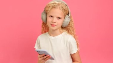 Sarışın beyaz kız kafasında bluetooth kulaklıklarla müzik dinlemeyi, dans etmeyi ve pembe stüdyo arka planında en sevdiği şarkıyı dinlemeyi seviyor..