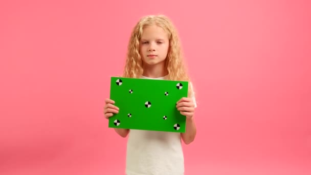 Ξανθιά κοπέλα κρατώντας πράσινο οθόνη Banner Σημεία Παρακολούθησης για Copy Space. Κενό πράσινο πίνακα οθόνης. Εμφανίζει μια εγκρίνοντας Thumbs-up χειρονομίες με χώρο για κείμενο ή διαφήμιση σε ροζ φόντο. — Αρχείο Βίντεο