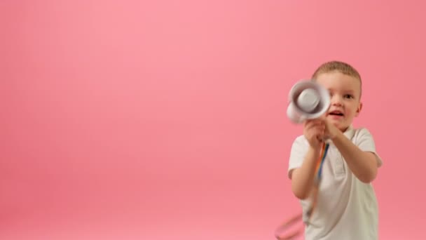 Slow motion porträtt glad blond vit pojke i vit skjorta håller megafon högtalare i händerna, vinka den åt sidorna och hoppa av glädje på rosa bakgrund med plats för reklam eller text. — Stockvideo
