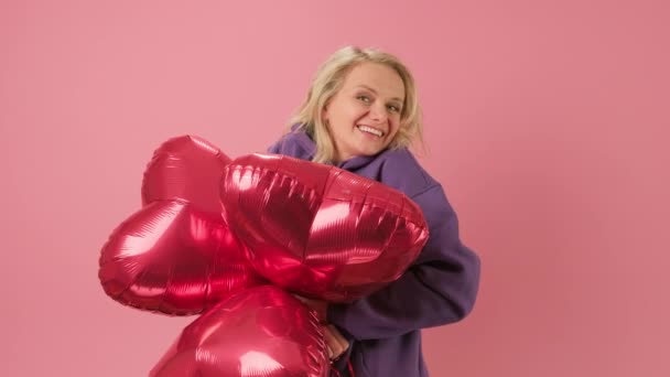 Portrait in slow motion of happy 30-year-old woman smiling and dancing, holding helium balloon with inscription I LOVE YOU, hiding behind balloons, congratulating on Mothers Day or Valentines Day. — Stock Video