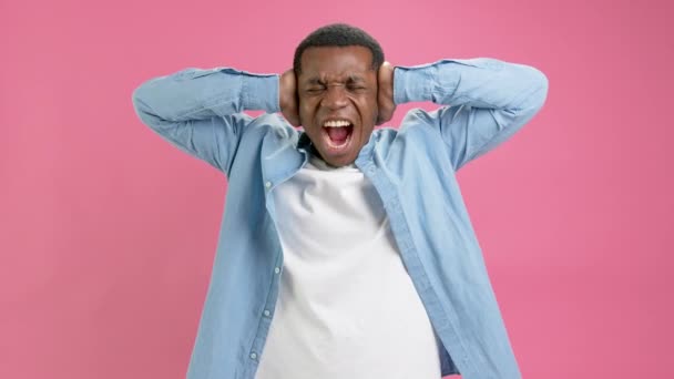 Porträtt missnöjd, irriterad, ledsen afroamerikansk man, slutna ögon, täcker öronen med händerna, inte vill lyssna, ropar isolerat på rosa studio bakgrund. En deprimerad man skriker. — Stockvideo