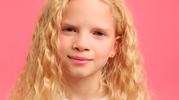 Närbild porträtt av allvarliga blonda tonåring flicka tittar in i kameran med allvarliga ansikte på rosa studio bakgrund. Porträtt 10-årig tonåring, flicka tittar in i kameran. — Stockvideo