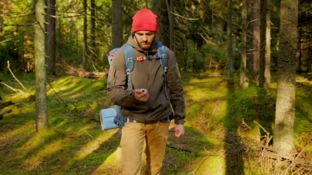 人は手にコンパスを持ち、方向を探します。地形上のオリエンテーリング。トレッキングコンセプト。観光客は森を移動するコンパスを使用します。森のパスに沿って大規模なバックパック旅行を持つ男. — ストック動画