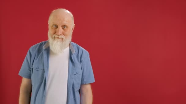 Old bearded man Holds Sign With Inscription Sale -40 off, Points His Finger at Empty Space Mock up and Looks at Discount in Camera and Smiles on Red Background. Μεγάλες εκπτώσεις τις μαύρες Παρασκευές. — Αρχείο Βίντεο