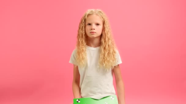 Σοβαρή ξανθιά κοπέλα κρατώντας Banner με πράσινο Screen Tracks σημεία για Copy Space. Κενό πράσινο πίνακα οθόνης. Δεν χαμογελά κοιτάζει κάμερα με χώρο για κείμενο ή διαφήμιση σε ροζ φόντο. — Αρχείο Βίντεο