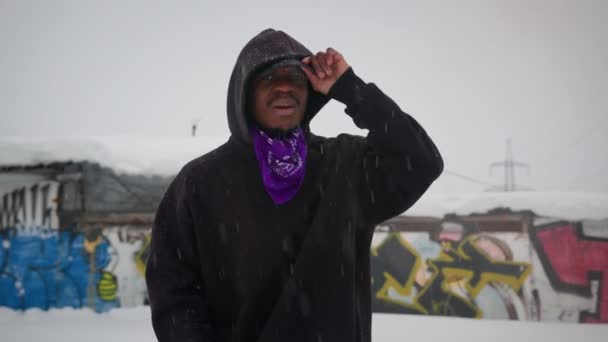 Slow-motion portret een Afro-Amerikaanse rapper zingen rap op straat in de winter sneeuwt het. Rapper zanger verkracht op straat in de winter, haast zijn handen en kijkt naar de camera. Straatkunst zwarte zanger. — Stockvideo