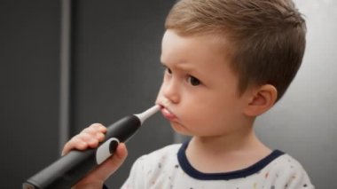 Oral hijyenle meşgul, ayakta duran ve aynaya bakan sarışın bir çocuk portresi. Küçük çocuk diş fırçasıyla dişlerini ve plaketini temizliyor. Diş macunuyla, aynanın önünde duruyor..