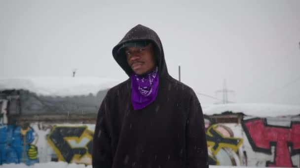 El rapero cantante rapea en la calle en invierno, se apresura a sus manos y mira a la cámara. Cantante negro de arte callejero. Retrato en cámara lenta un rapero afroamericano cantando rap en la calle en invierno nieva. — Vídeos de Stock