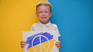Ukrayna bayrağının sarı-mavi arka planında ağlayan çocuk Ukrayna bayrağının renginde barış sembolü taşıyor. Savaşa karşı çocuk, kriz Ukrayna, insani felaket, Rus saldırganlığı.