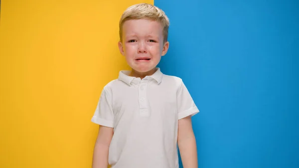 Retrato pequeño niño rubio llorando sobre la bandera de fondo amarillo-azul de Ucrania. Crisis en Ucrania, guerra contra los niños, agresión rusa catástrofe humanitaria, asistencia a los niños en Ucrania. — Foto de Stock