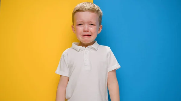 Retrato pequeno menino loiro chorando na bandeira de fundo amarelo-azul da Ucrânia. Crise na Ucrânia, guerra contra as crianças, agressão russa catástrofe humanitária, assistência às crianças na Ucrânia. — Fotografia de Stock