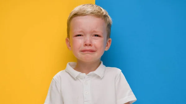 Retrato pequeño niño rubio llorando sobre la bandera de fondo amarillo-azul de Ucrania. Crisis en Ucrania, guerra contra los niños, agresión rusa catástrofe humanitaria, asistencia a los niños en Ucrania. — Foto de Stock