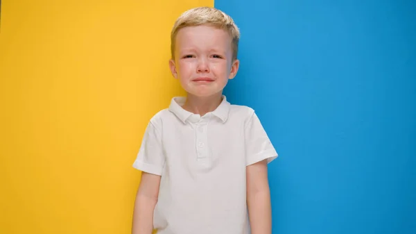 Retrato pequeño niño rubio llorando sobre la bandera de fondo amarillo-azul de Ucrania. Crisis en Ucrania, guerra contra los niños, agresión rusa catástrofe humanitaria, asistencia a los niños en Ucrania. — Foto de Stock
