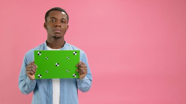Ciddi Afro-Amerikalı Banner 'ı Yeşil Ekran Kopyalama Noktaları ile tutuyor. Boş Yeşil Ekran Panosu. Gülümseme, Pembe Arkaplanda Metin veya Reklamcılık İçin Kameraya Bakmaz.