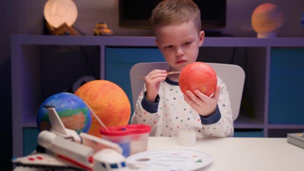 Niño rubio pintar planeta sistema solar Mercurio con pintura colorida mesa de estar en casa por la noche, planeta sistema solar, naves espaciales y transbordador espacial de constructor alrededor. Día de la Cosmonáutica el 12 de abril. — Vídeos de Stock