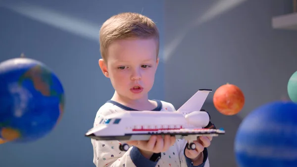 かわいい男の子は、太陽系の惑星の間で宇宙を飛んで、おもちゃのスペースシャトルで遊んでいます。太陽系の空間を飛ぶスペースシャトルで自宅で遊んでいる子供。4月12日の宇宙の日. — ストック写真
