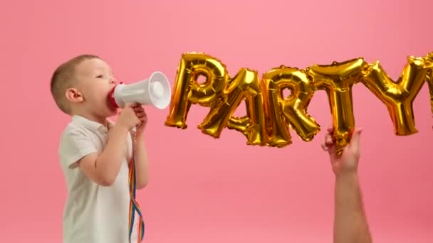 Child is having fun shouting into loudspeaker against background of word PARTY. Boy jumps for joy holding megaphone in his hands and shouts into loudspeaker against background of inscription party. — Vídeos de Stock