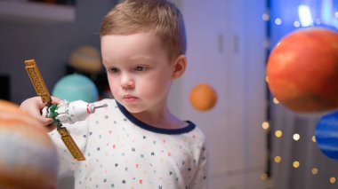 Sarışın çocuk uzay uydusuyla oynuyor. Yapımcı tarafından yapılmış. Güneş sistemi yakınlarında uzayda uçuyor. Çocuk uzay mekiğinde uçmak için astronot olmayı hayal ediyor. Uzay Günü 12 apr.