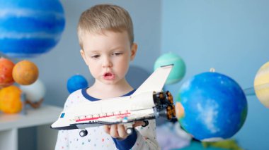 Portre çocuk oyuncak uzay mekiğiyle oynuyor, güneş sistemi gezegenleri arasında uzayda uçuyor. Çocuk evde uzay mekiğiyle oynuyor. Güneş sisteminde uzayda uçuyor. 12 Nisan Kozmonotlar Günü.