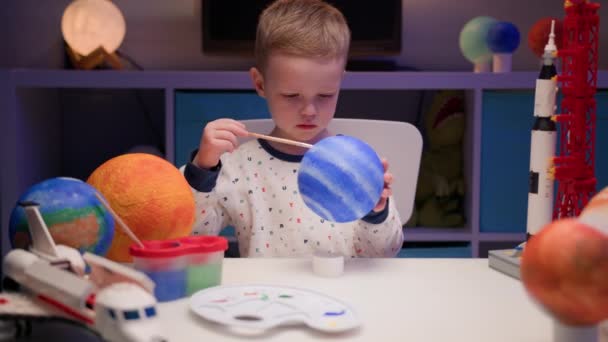 Blond pojke måla planeten solsystemet Neptunus med färgglada färg sitter hemma bord på kvällen, planet solsystem, rymdskepp och rymdfärja från konstruktör runt. Kosmonautisk dag den 12 april. — Stockvideo