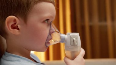 Blond caucasian child with asthma problems does inhalation with mask on his face. Baby has respiratory infection or bronchitis and is breathing heavily. Treatment pneumonia with nebulizer at home.
