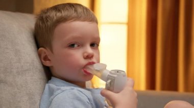 Child has respiratory infection or bronchitis, and he is breathing heavily. Blond Caucasian child with asthma problems inhales with tube in his mouth. Treatment of pneumonia with nebulizer at home.