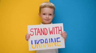 Portre Sarışın çocuk Ukrayna 'nın yanında durmak için sesleniyor, yazıyla bayrağı kaldırıyor Ukrayna' daki savaşı durdurun mavi-sarı stüdyo arka planında duruyor. Savaş yok, savaşı durdurun, Rus saldırıları.