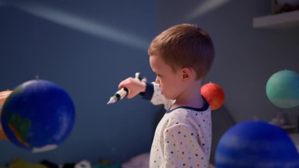 Menino loiro está brincando com foguete espacial de brinquedo, voando no espaço entre planetas do sistema solar. Criança está brincando em casa com foguete voando no espaço do sistema solar. Dia da Cosmonáutica em 12 de abril. — Vídeo de Stock