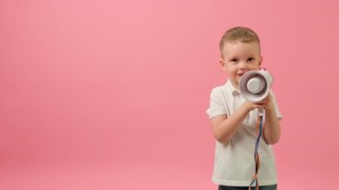 Boy rallies with loudspeaker on pink background. Blond caucasian 5-year-old child in white T-shirt shouts into megaphone and agitates for purchase of goods at sale with a big discount on Black Friday.