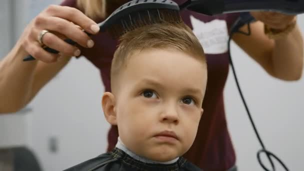 Blow-drying hair for little boy, hair styling, fashionable haircut in barber shop by master stylist. Close-up of process of drying hair of child in barber shop. — Video