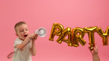 Boy jumps for joy holding megaphone in his hands and shouts into loudspeaker against background of inscription party. Child is having fun shouting into loudspeaker against background of word PARTY.