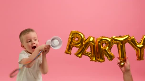 Dreng hopper af glæde holder megafon i hænderne og råber i højttaler på baggrund af indskrift fest. Barnet har det sjovt med at råbe ind i højttaleren på baggrund af ordet PARTY. – Stock-video