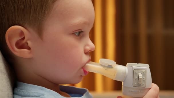 Portrait caucasian child with asthma problems inhales with tube in his mouth. Treatment of pneumonia with nebulizer at home. Child has respiratory infection or bronchitis, and he is breathing heavily. — Wideo stockowe