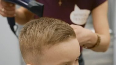 Close-up of process of drying hair of child in barber shop. Blow-drying hair for little boy, hair styling, fashionable haircut in barber shop by master stylist.
