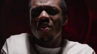 Portrait African-American guy singing song rapping on red underground background. Black guy in white T-shirt raps, sings song waving his arms. Rap artist, recording rap or hip hop music video.