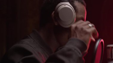 African American man singer takes off his white headphones and hangs them on stand with microphone. Black man rap singer in recording studio takes off his headphones, finishes recording music track.