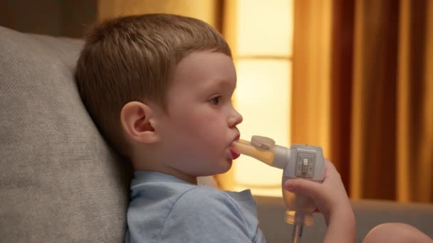 Treatment of pneumonia with nebulizer at home. Child has respiratory infection or bronchitis, and he is breathing heavily. Blond Caucasian child with asthma problems inhales with tube in his mouth. — Stockvideo