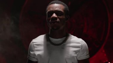 Portrait black African American man hip hop singer singing rap song in white t-shirt on red background. Black man teenage hip hop artist raps and waves his arms while recording music video for song.