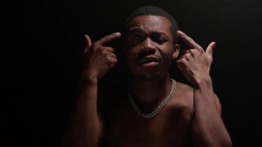 Shooting clip of rap artist. Man sings rapping song. Handsome black African American man with pumped naked torso sings song emotionally waving his arms on black background.