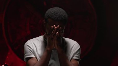 Portrait African American guy is experiencing from occurrence of tragedy in life, covering his hands with his face and praying with his hands folded in front of him put hands praying with hope concept