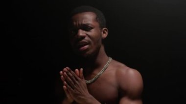Shooting clip of rap artist. Man sings rapping song. Handsome black African American man with pumped naked torso sings song emotionally waving his arms on black background.