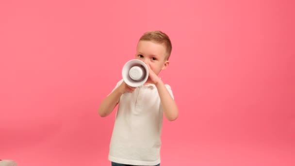 Blonde Caucasian boy jumps with megaphone on pink background. Child jumping with loudspeaker agitates for sale on Black Friday or cyber Monday — стоковое видео