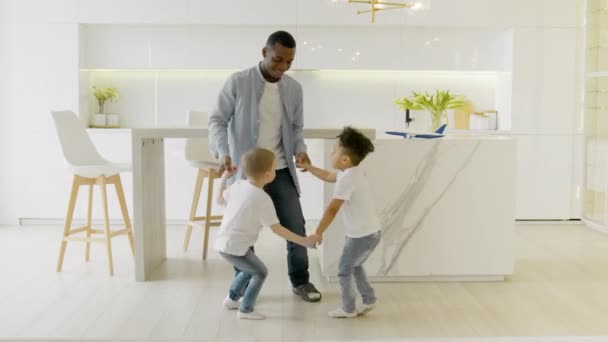 Multiracial dancing of black man with two children of Caucasian origin and mix race in kitchen of house. Having fun in multiracial family. Children dancing with their father in kitchen. — Stockvideo
