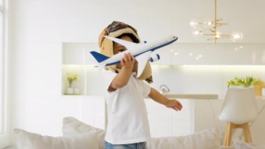 Cute 3 year old African American child in glasses and pilot hat plays at home with toy modern airplane, child dream becoming pilot, thirst for travel, tourism and air travel. Kid play air craft toy.