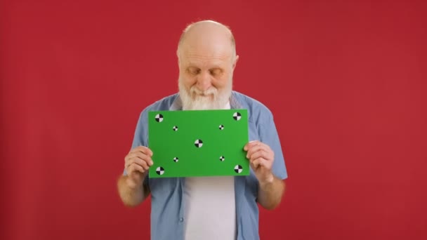Vieil homme heureux tenant la bannière avec l'écran vert suit les points pour l'espace de copie. Panneau d'écran vert vide. Happy dance et réjouir avec de l'espace pour le texte ou la publicité sur fond rouge. — Video