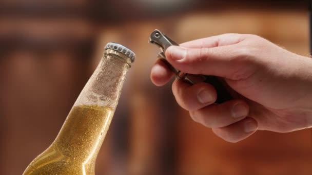 Close-up caucasian man hand opens lid fresh light beer in glass bottle with lid opener on blurry studio background. Slow-motion video of light lager is opened with the help of bottle opener. — Video